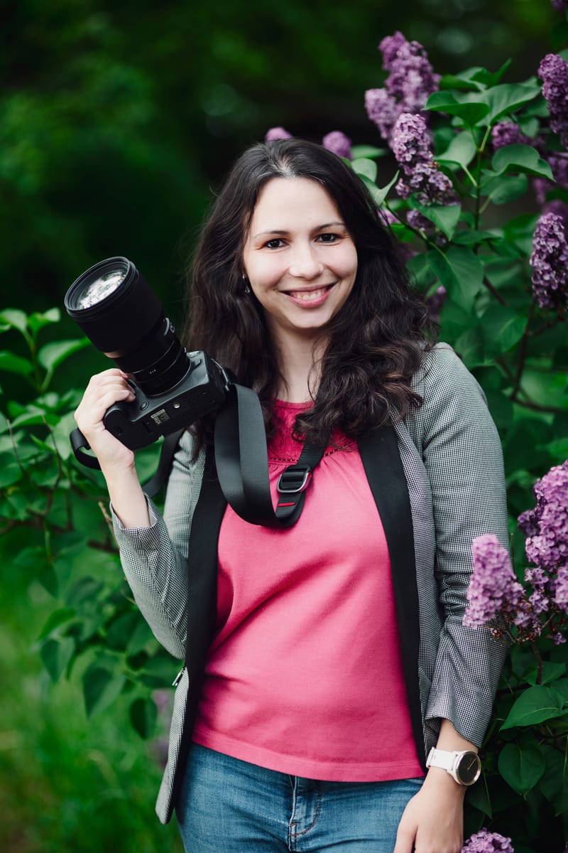 Fotografka Nikolka Světinská s fotoaparátem v ruce se usmívá mezi kvetoucími šeříky