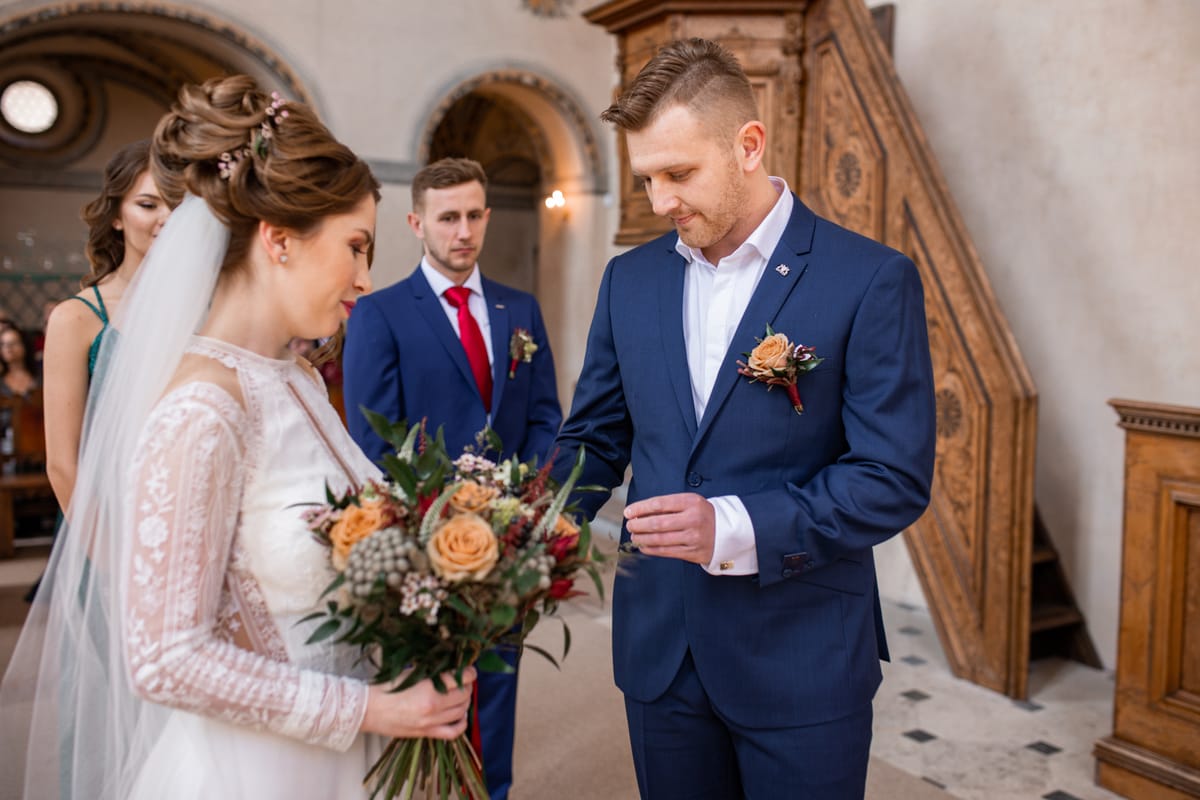Ženich v modrém obleku drží prstýnek, naproti stojí nevěsta s podzimní kyticí